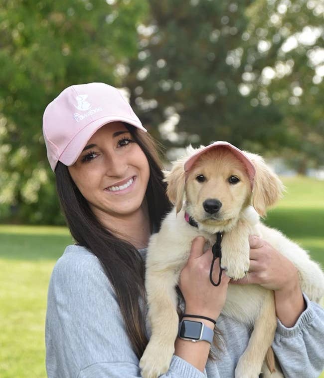 image of reviewer holding up a puppy, both of them wearing matching pink baseball hats