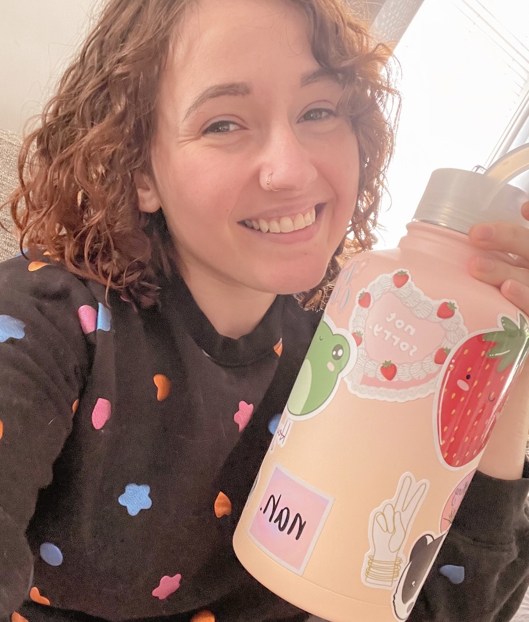 A person smiling while holding a pink water bottle with stickers on it