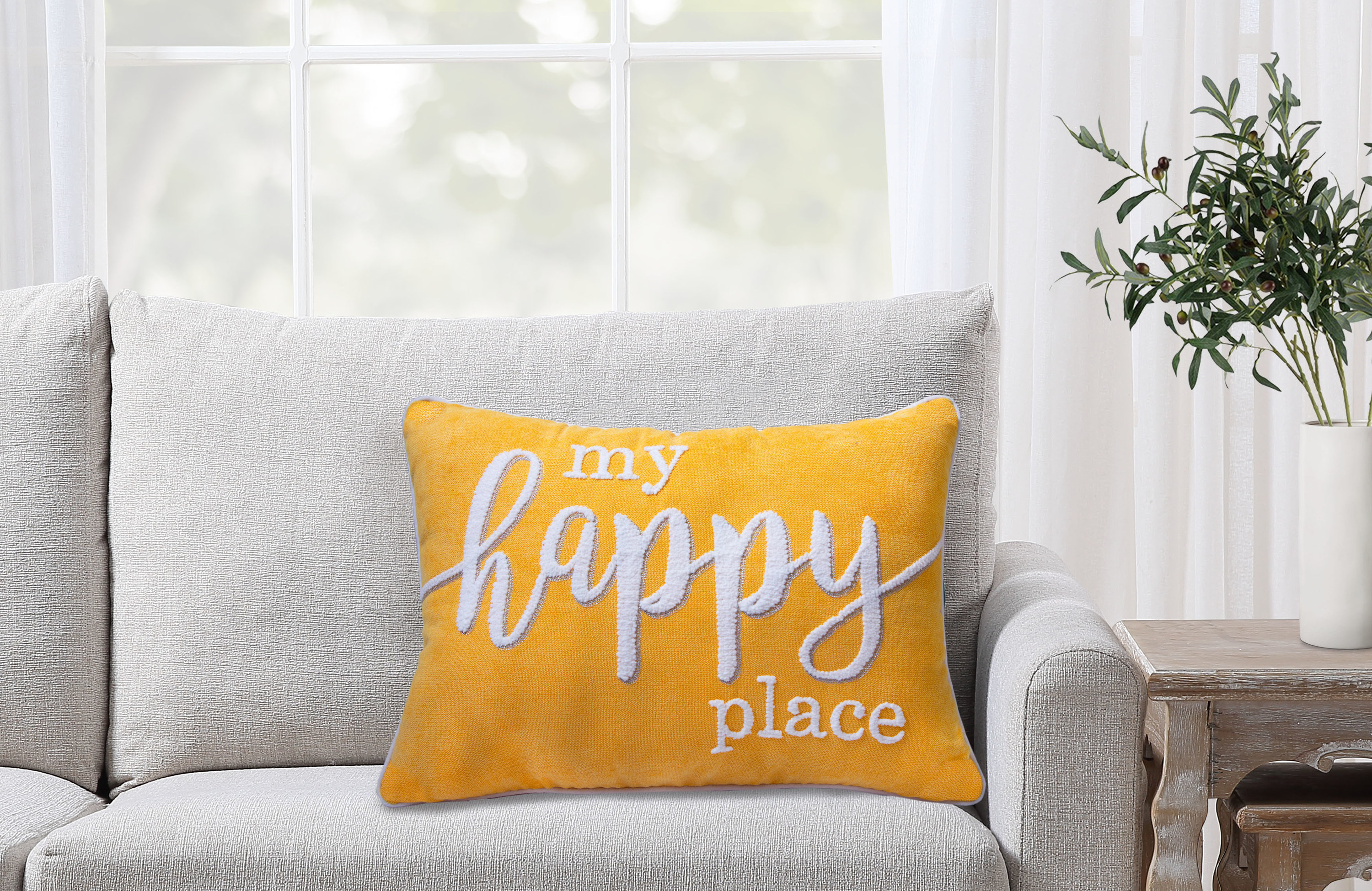 A bright yellow pillow that reads "my happy place" on a couch