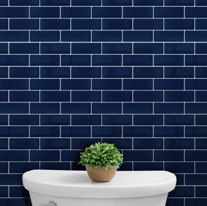 Dark blue peel & stick subway tiles over a toilet with a plant on its lid