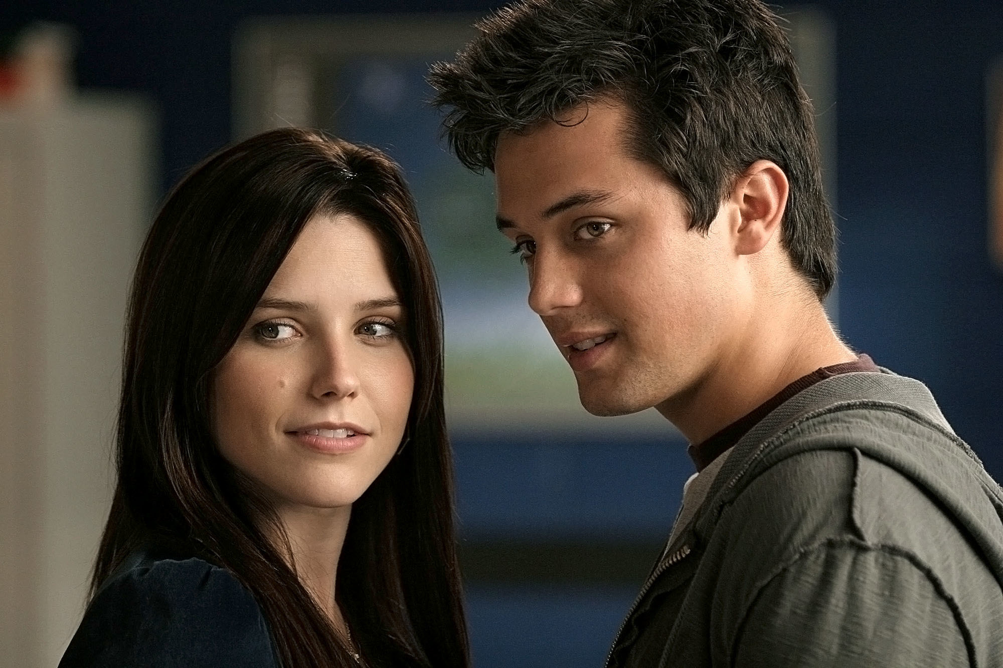 On the set of One Tree Hill, actors Sophia Bush and Stephen Colletti smirk, both looking off to the left