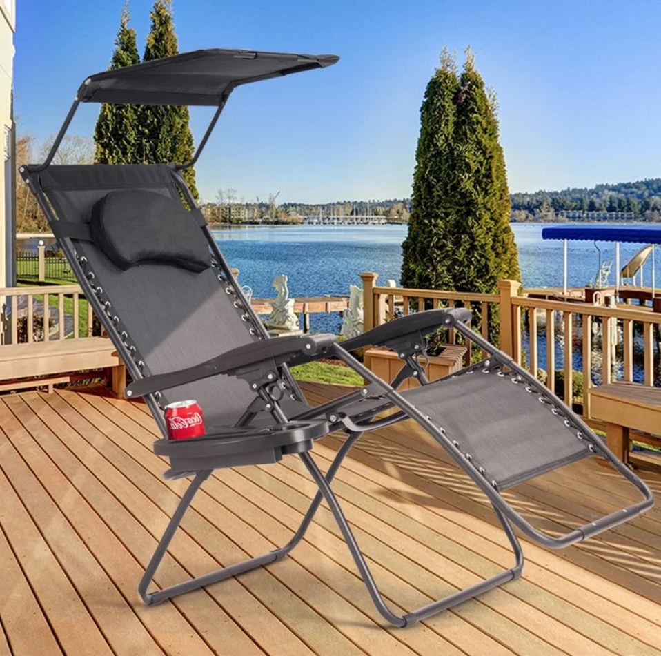 A grey, reclining outdoor chaise with a removable pillow and an umbrella on a deck
