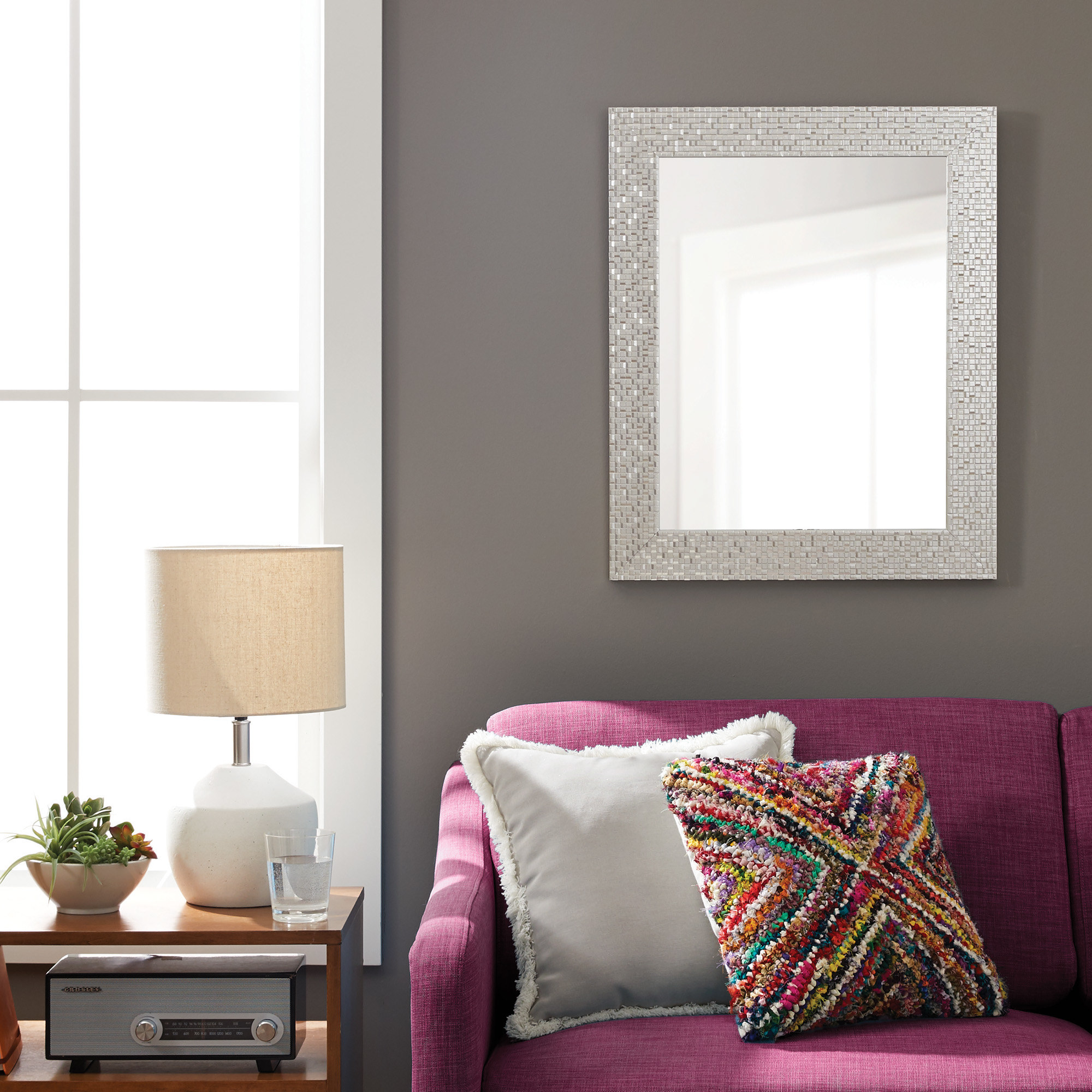 A silver mosaic mirror hanging over a magenta couch
