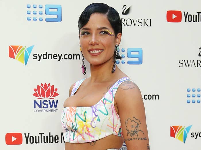 Halsey smiles on a red carpet in a white crop top with colorful squiggles 