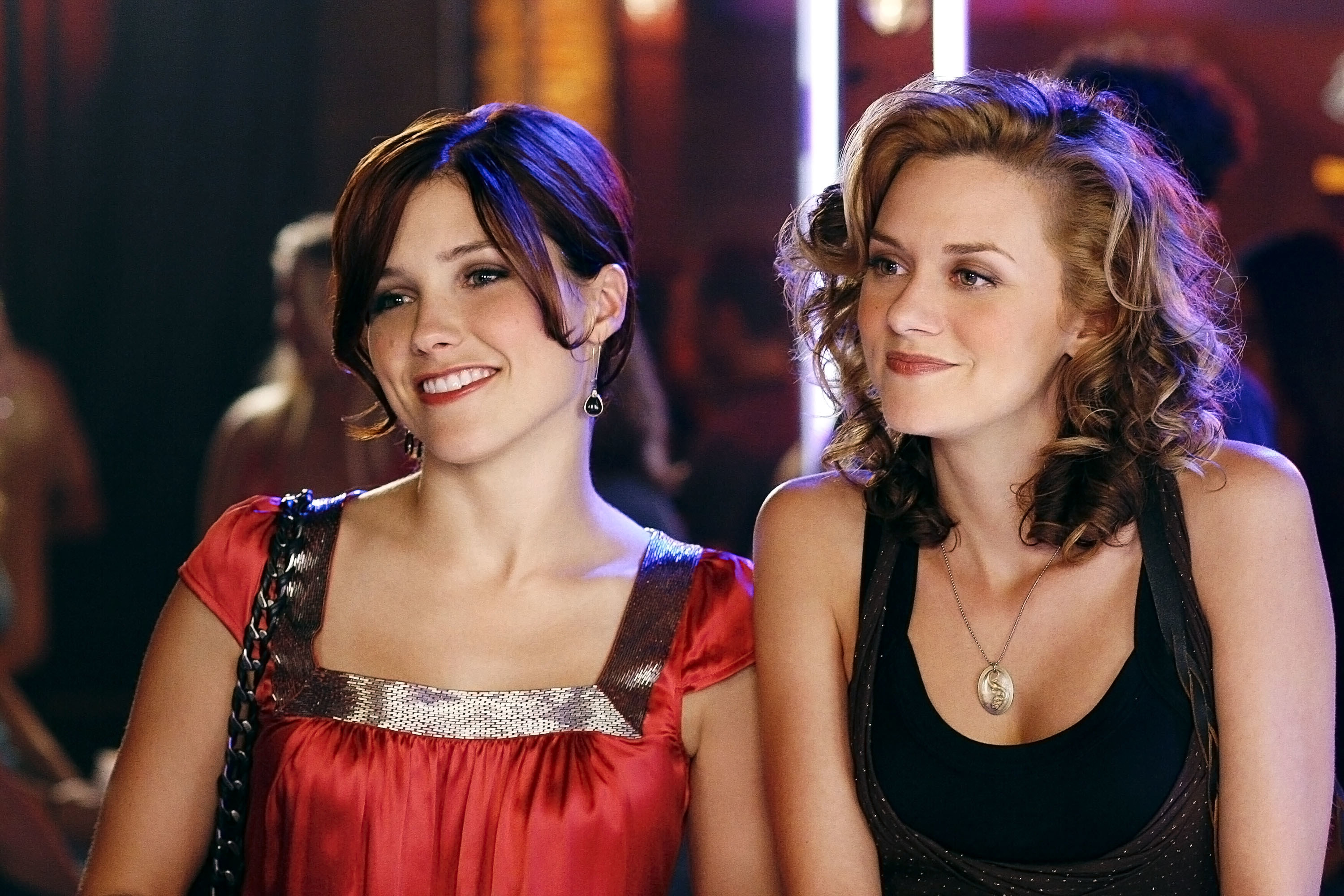 On set of One Tree Hill, actors Sophia Bush and Hilarie Burton smile, dressed up in club attire