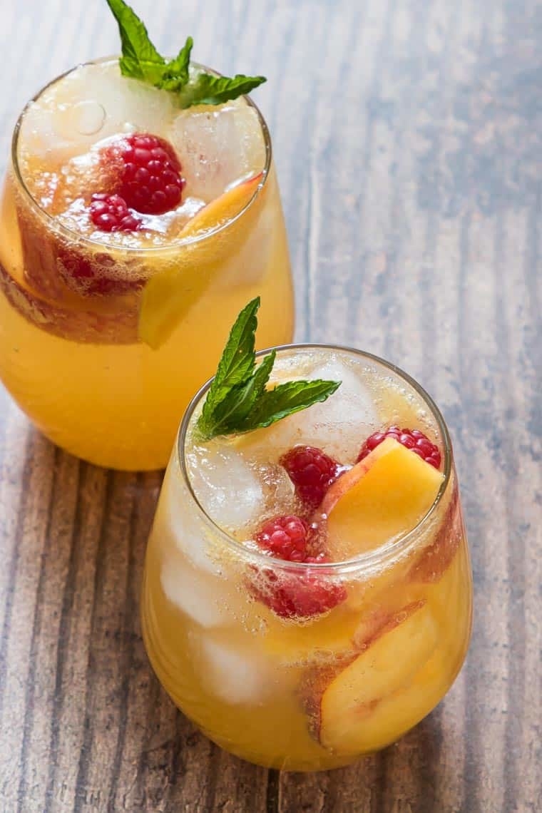 Two bourbon peach smash cocktails topped with mint and raspberries.