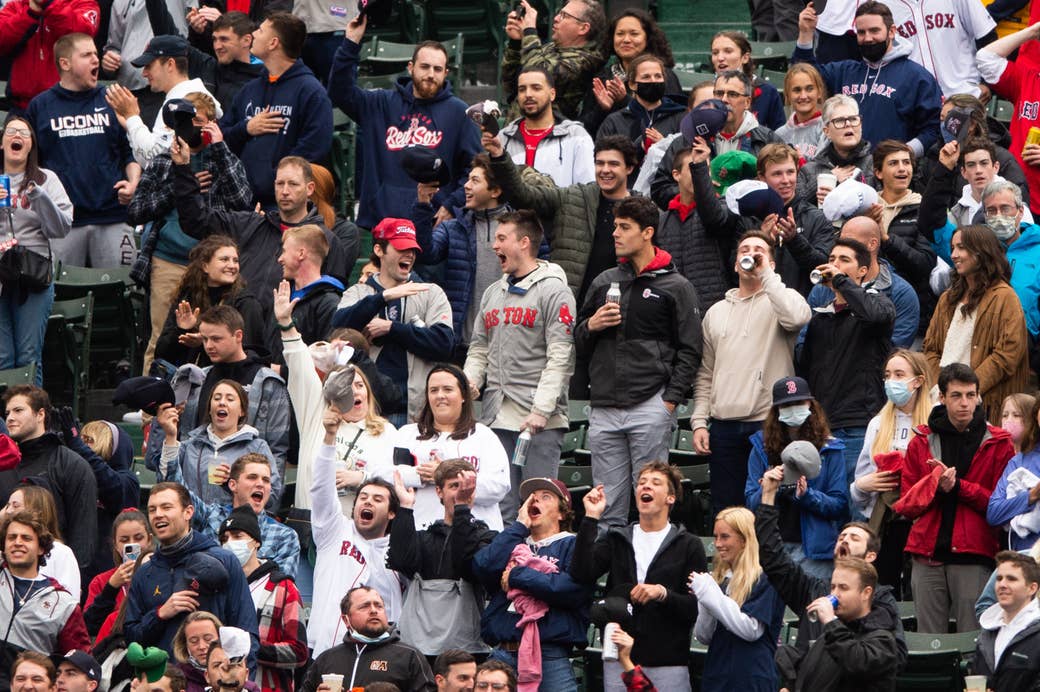 A crowd of people, most unmasked, wearing Boston sports gear in the stands at Fenway Park 