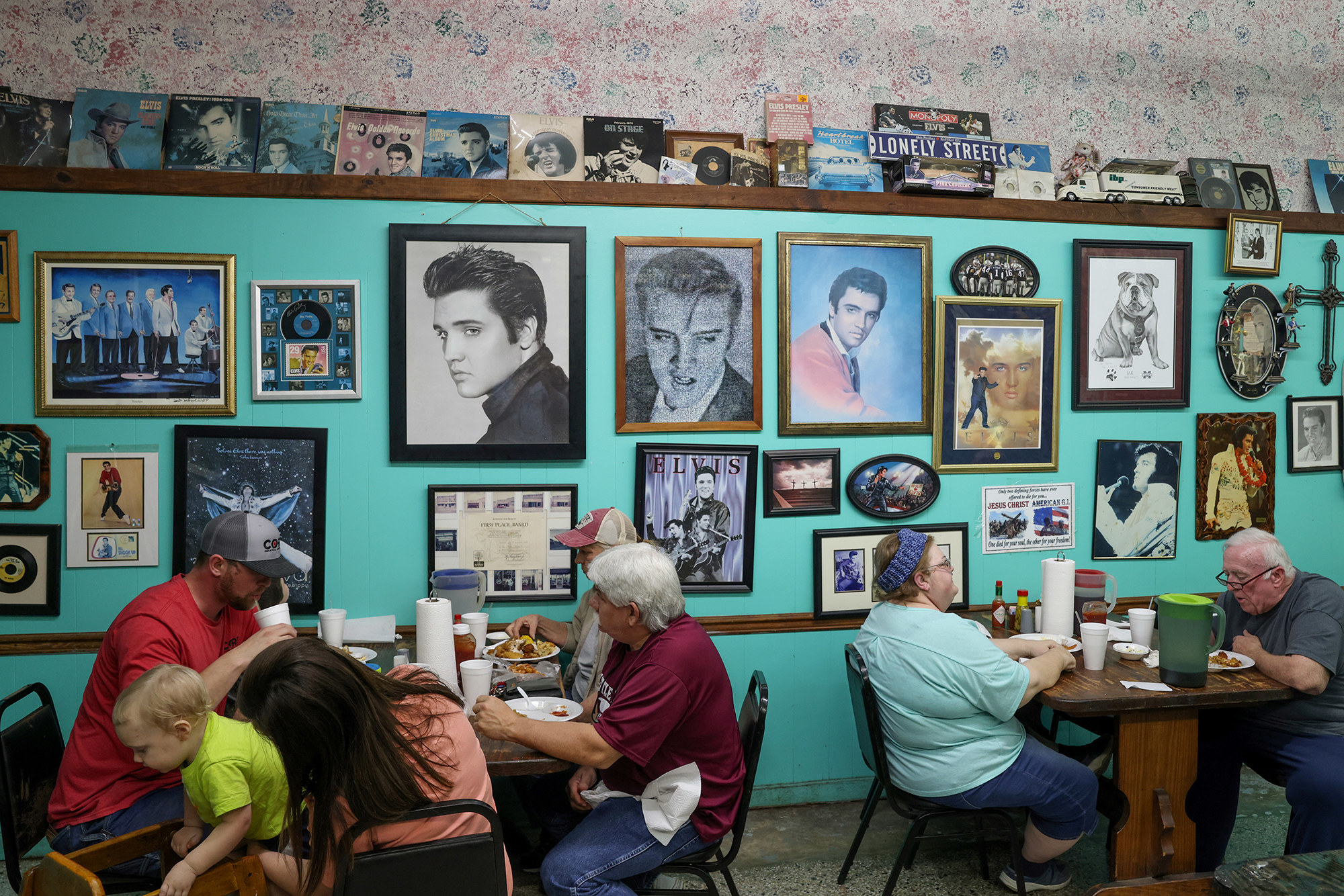 People gather maskless indoors at a restaurant with many pictures of Elvis on its walls