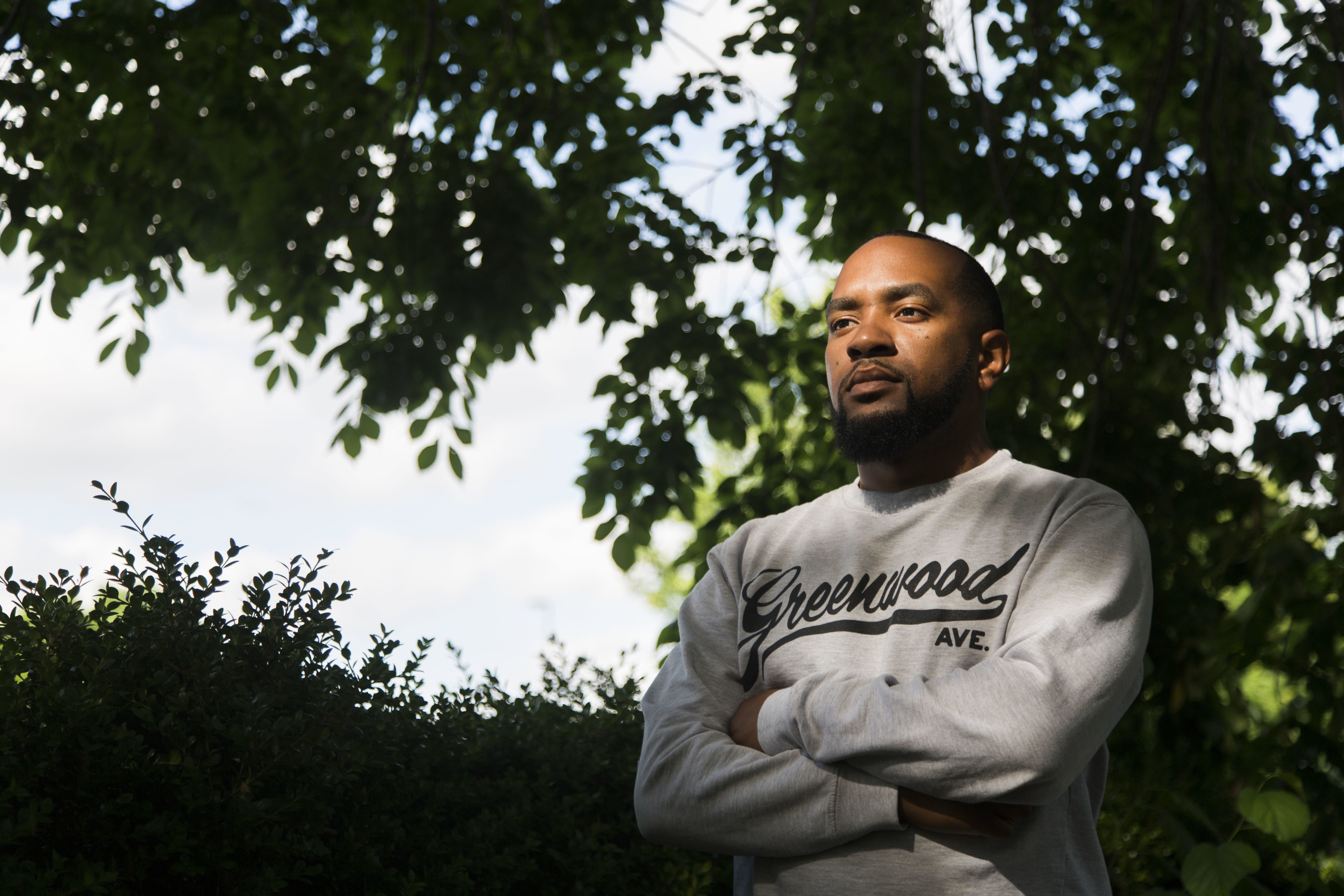 A man stands under a tree wearing a sweatshirt that reads &quot;Greenwood Ave&quot;