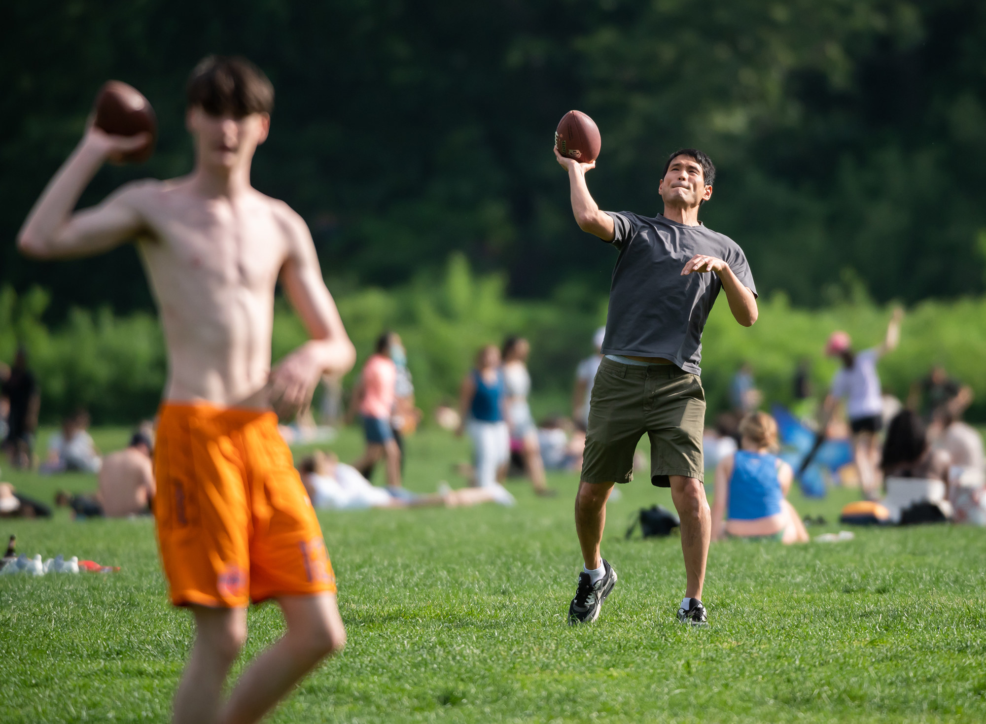 Two men in shorts throw footballs past the camera