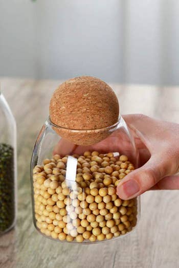 Person holding small glass canister with round cork lid 