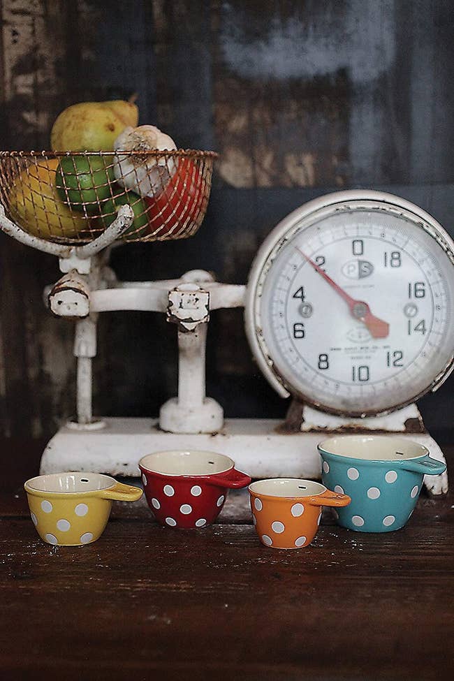 Four polka dot measuring cups in front of a decorative cooking scale