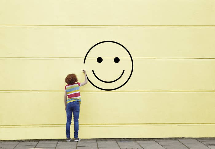 A person in jeans and a striped t-shirt painting a smiley face on a wall