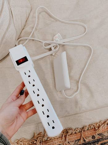 a reviewer photo of  a hand holding the outlet cover with a power strip attached 