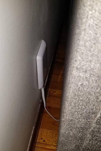 a reviewer photo of the slim outlet cover with a piece of furniture up against the wall 