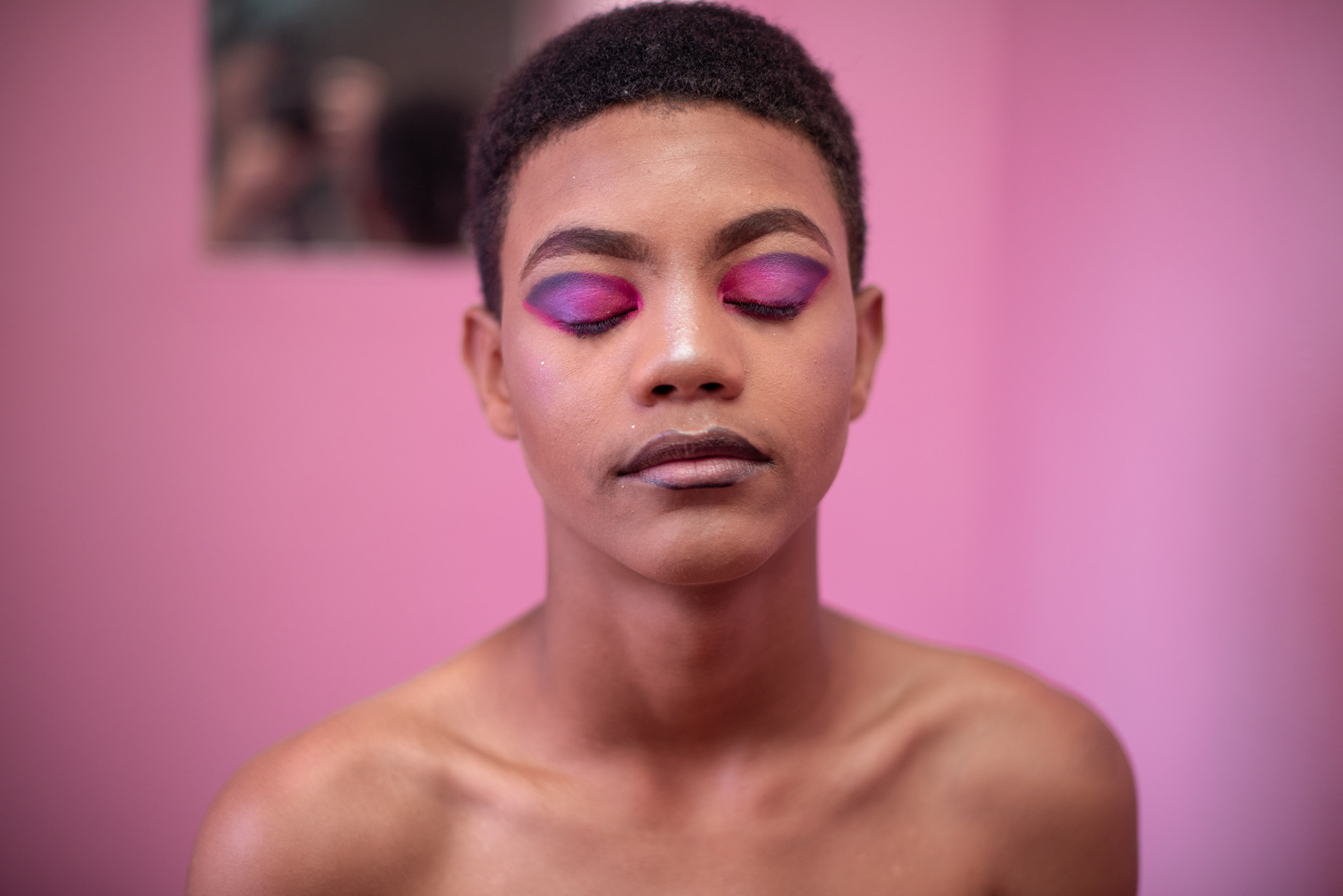 Person with closely cropped hair and closed eyes revealing colorful, bold eyeshadow