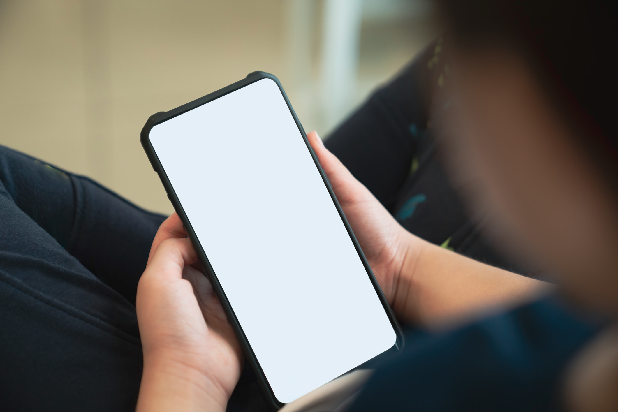 Over-the-shoulder view of someone sitting cross-legged holding a large phone/tablet in their hands that is totally blank