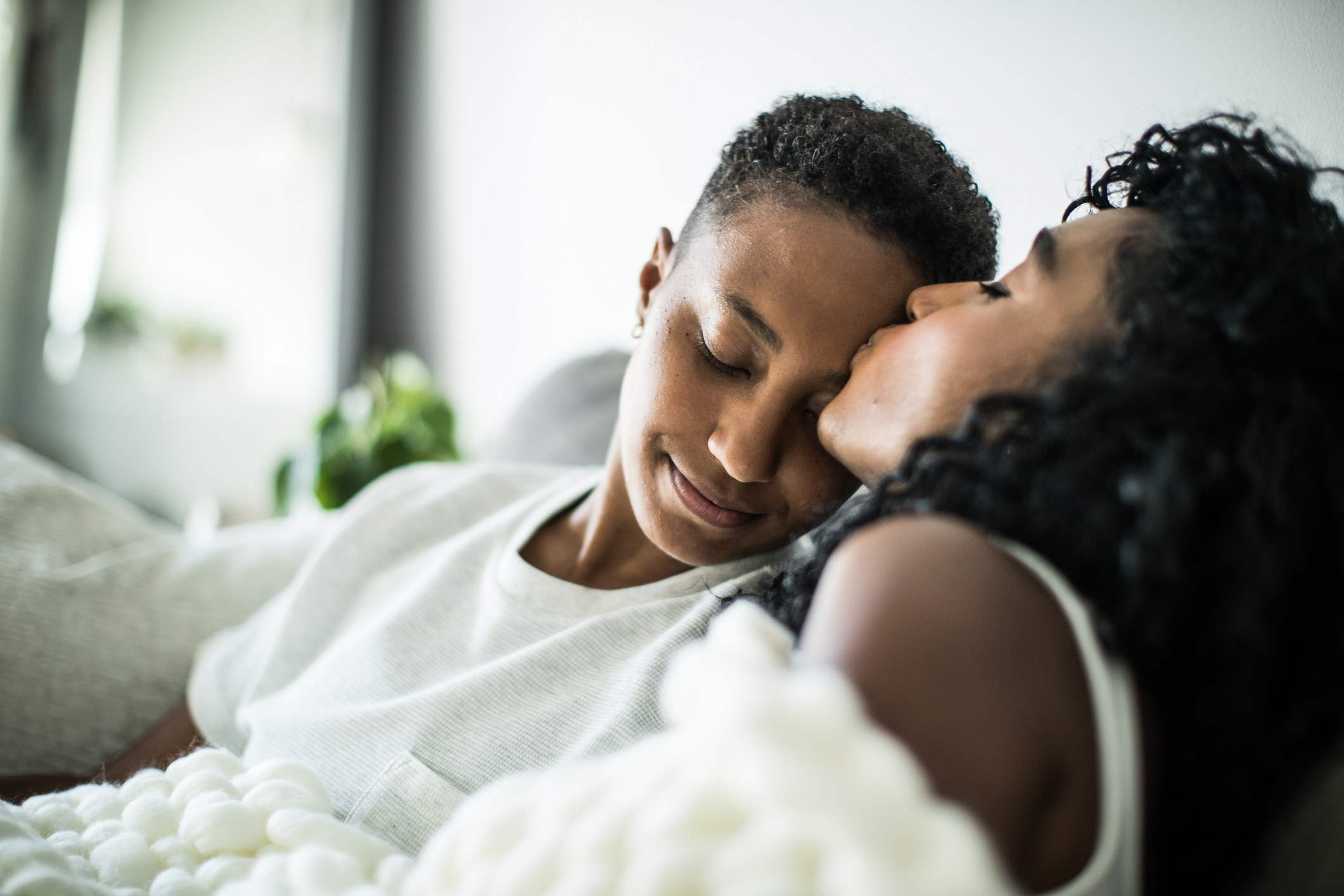 Two people lounging on an couch, one kissing the other on the forehead