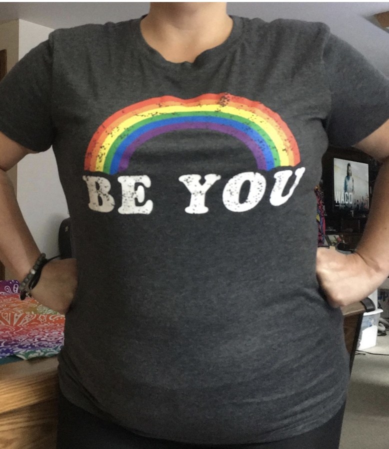 A reviewer wearing a grey graphic rainbow tee