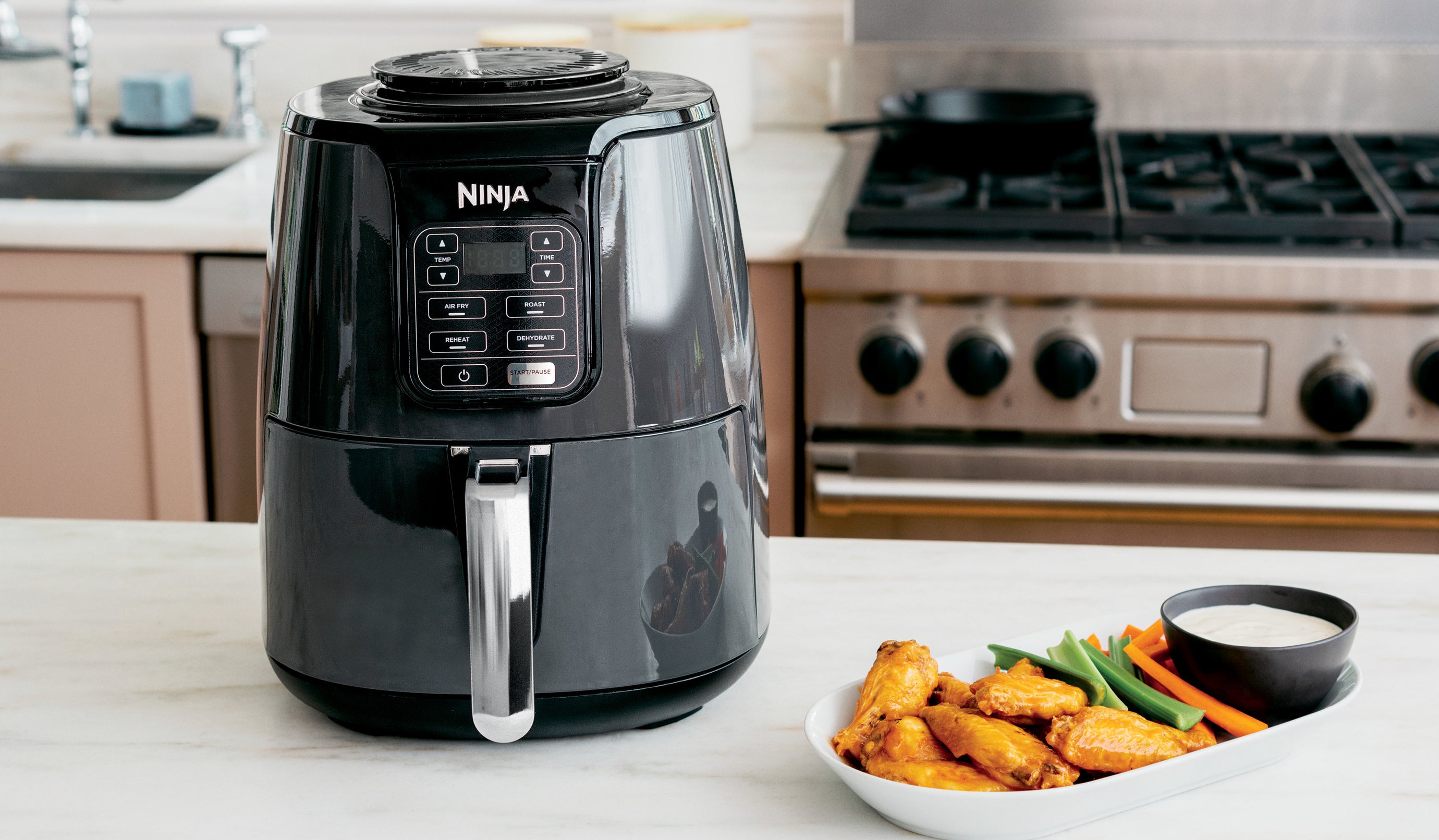 black air fryer on a counter next to a plate of chicken wings