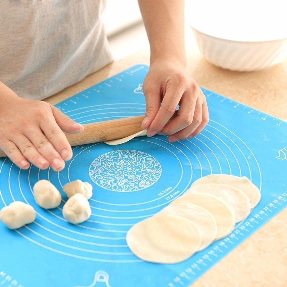 A person making rotis on a blue non stick silicone mat.