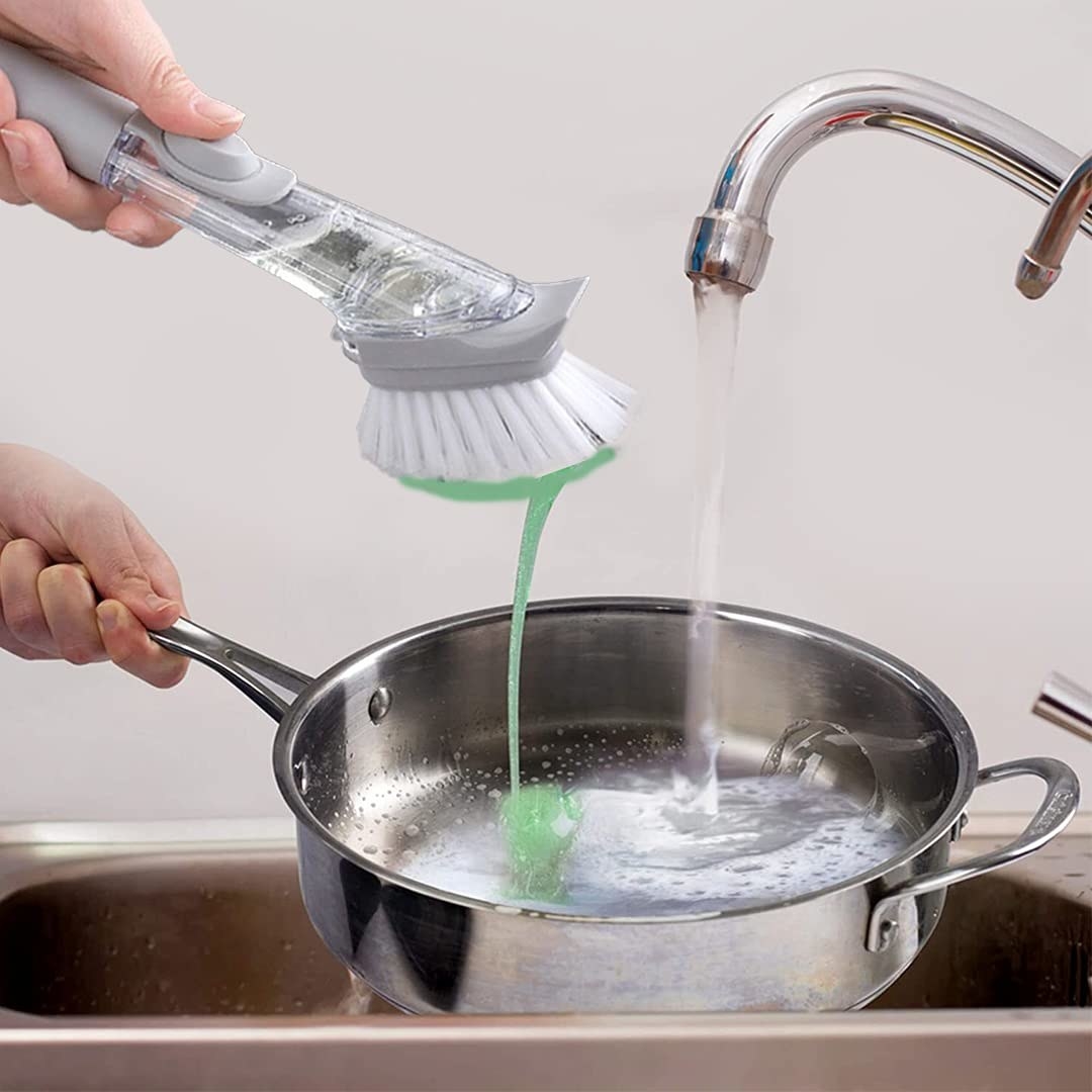 A 2-in-1 dishwashing brush and soap dispenser cleaning a utensil.