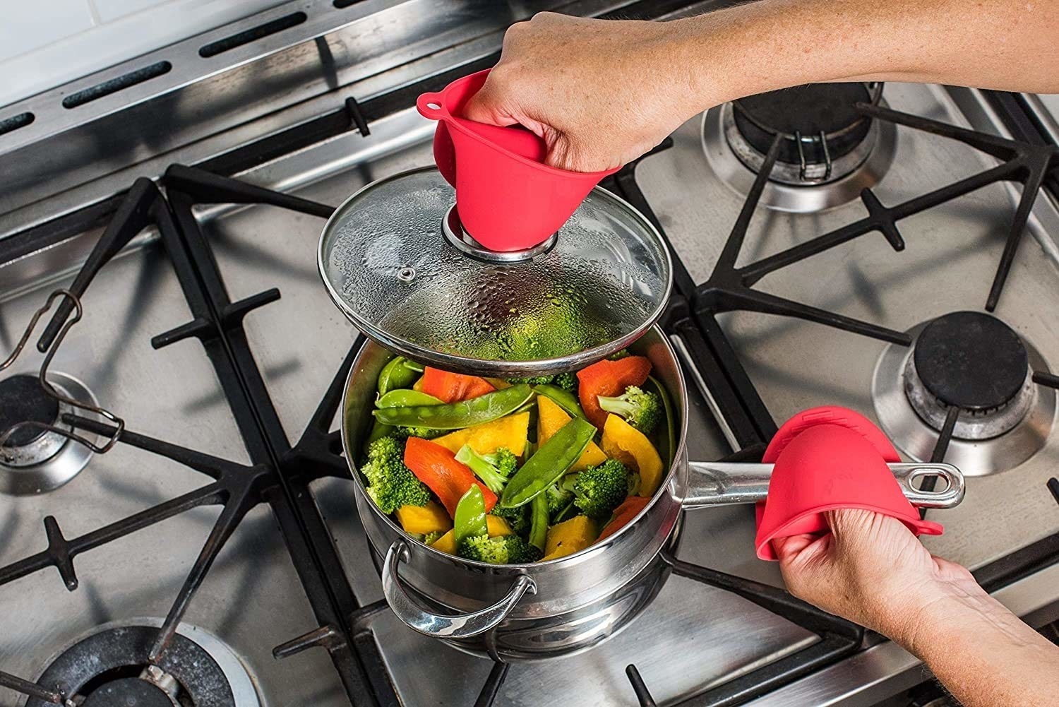 A person using silicone mitts to open the lid of a pot on a stove.