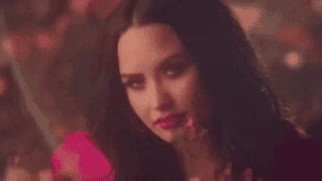 A gif of Demi Lovato holding flowers, looking directly into the camera, and then looking away