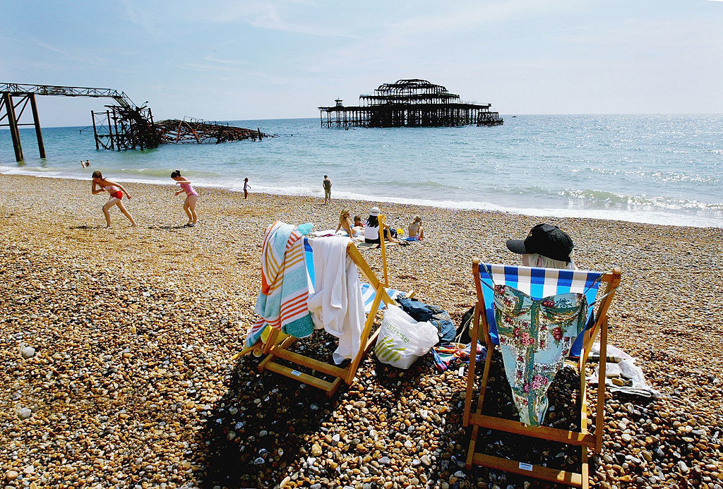 People relaxing in chairs by the beach while children play in the distance