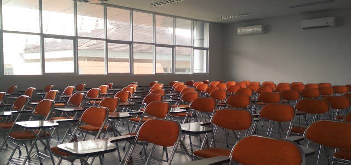 An empty classroom with rows of chairs and desks. 