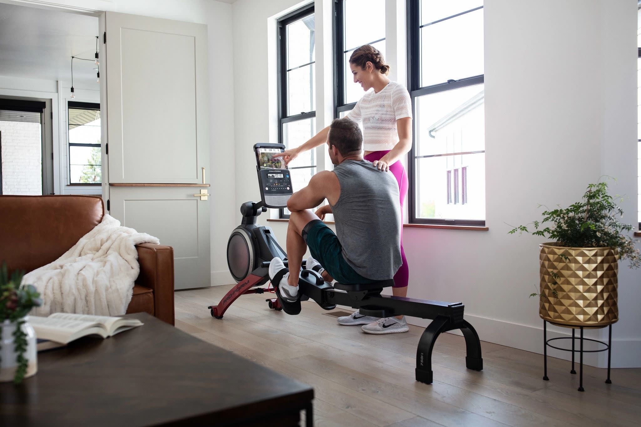 a person sitting on the rowing machine with another person showing them how to use it