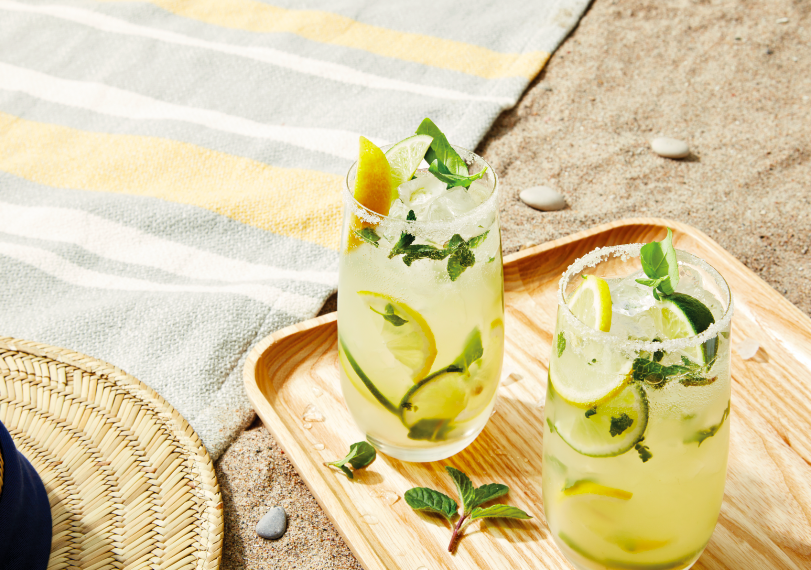 Two summer cocktails with citrus and mint leaves on a tray on a beach