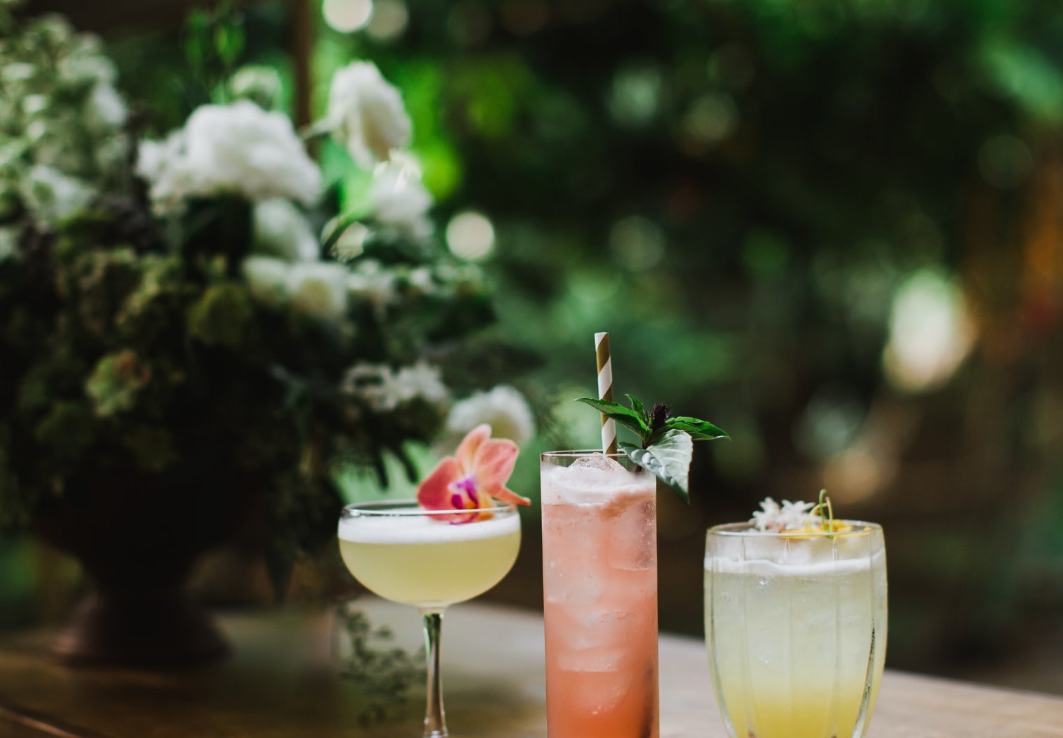Three beautiful cocktails on a bar beside a bouquet of flowers