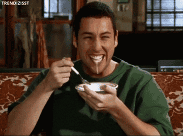 Adam Sandler laughing very hard while eating cereal.