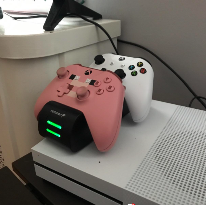 the black charging station with two pink and white Xbox controllers on top it charging