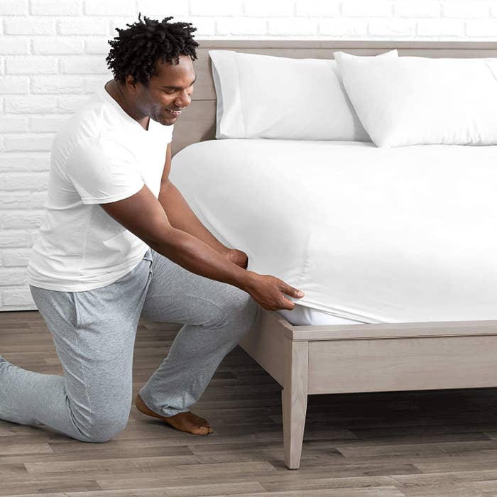 model in their pajamas pulling a white fitting sheet over the mattress