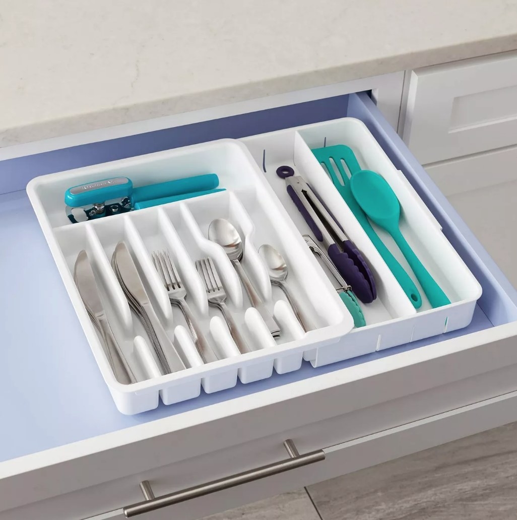 An expandable utensil tray in white filled with utensils inside a kitchen drawer