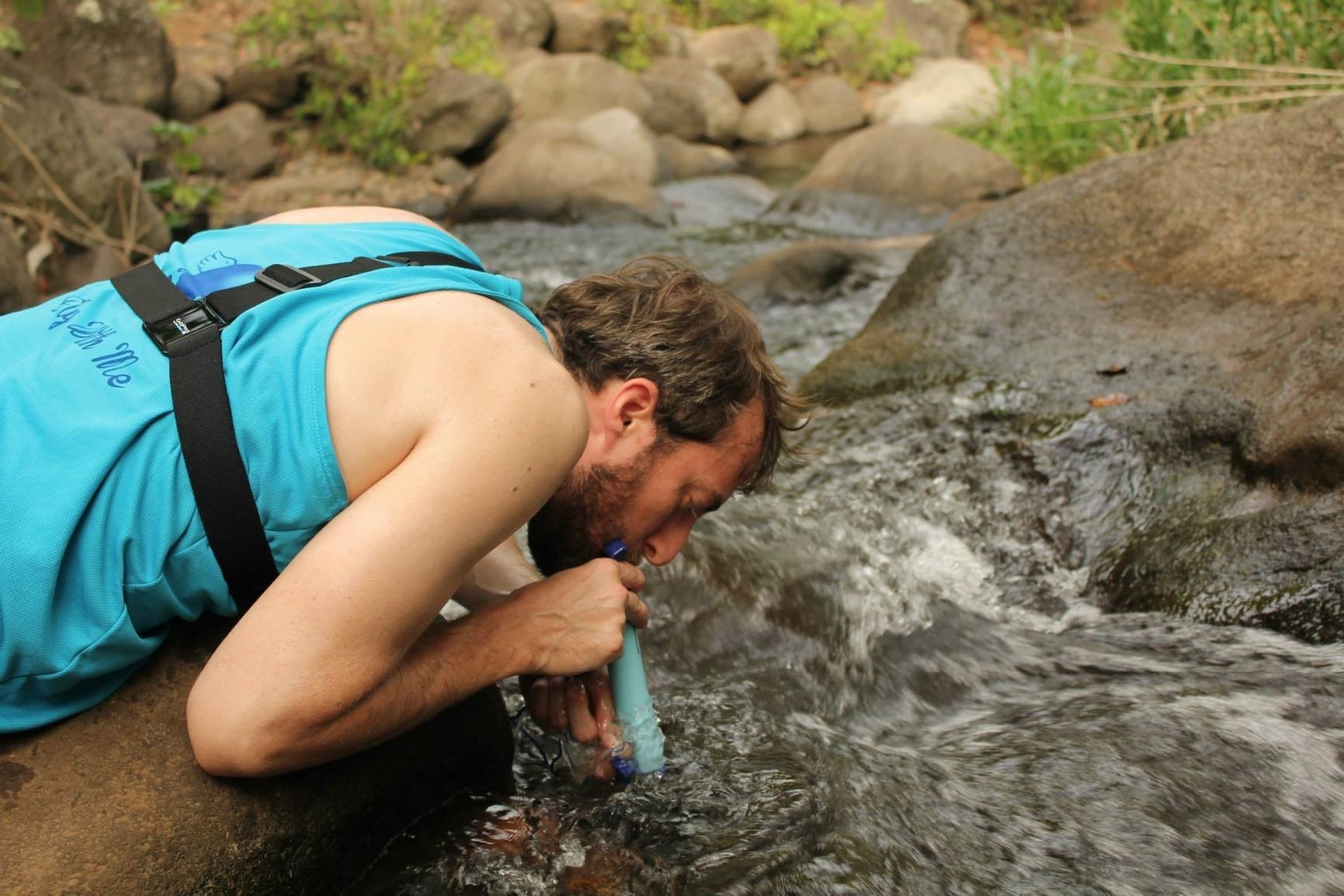 Reviewer is drinking water from a river using a Lifestraw