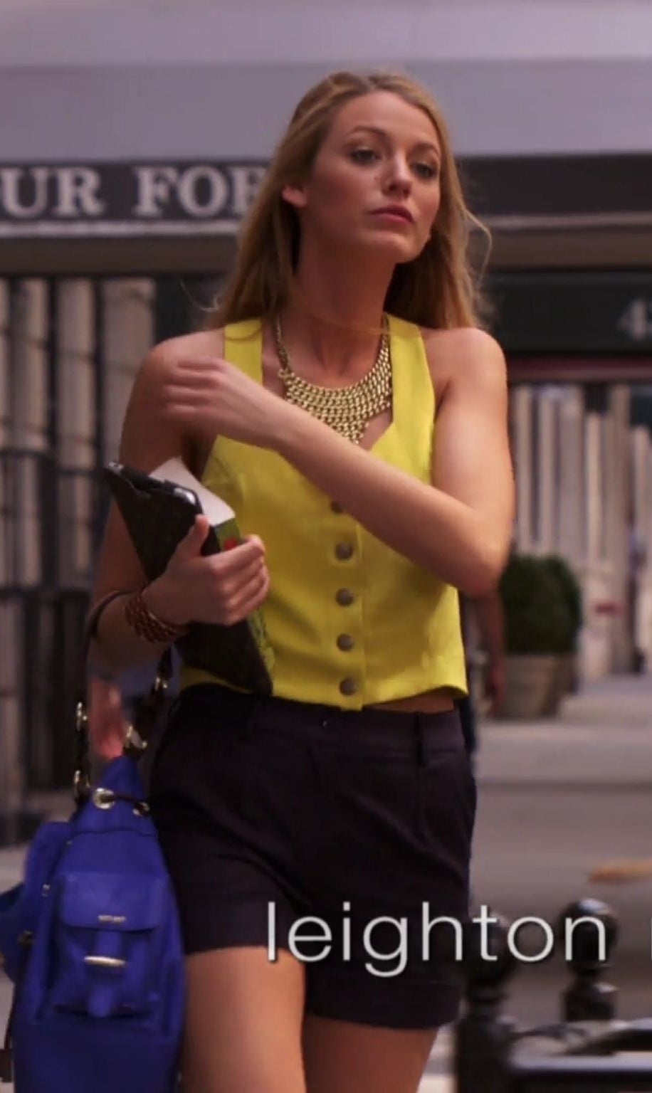 Serena in a sleeveless button up vest with high waisted shorts and a big chain necklace