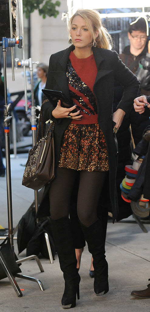 Serena in tights, a floral short flare skirt with sequins at the bottom and a long sleeve sweater with a sequin shooting star pattern and a long peacoat with high suede boots