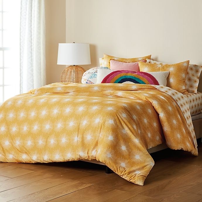 A yellow comforter with sunburst patterns on a bed.