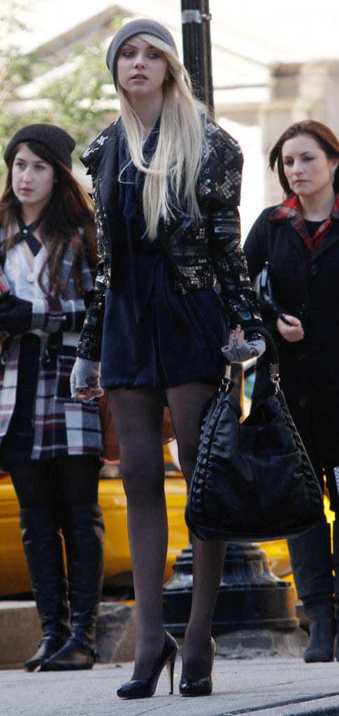 Jenny in heels and tights with a dark minidress, a scarf, kand a studded moto leather jacket and a beanie
