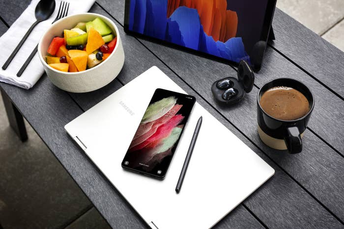 A laptop and phone next to a bowl of fruit and cup of coffee