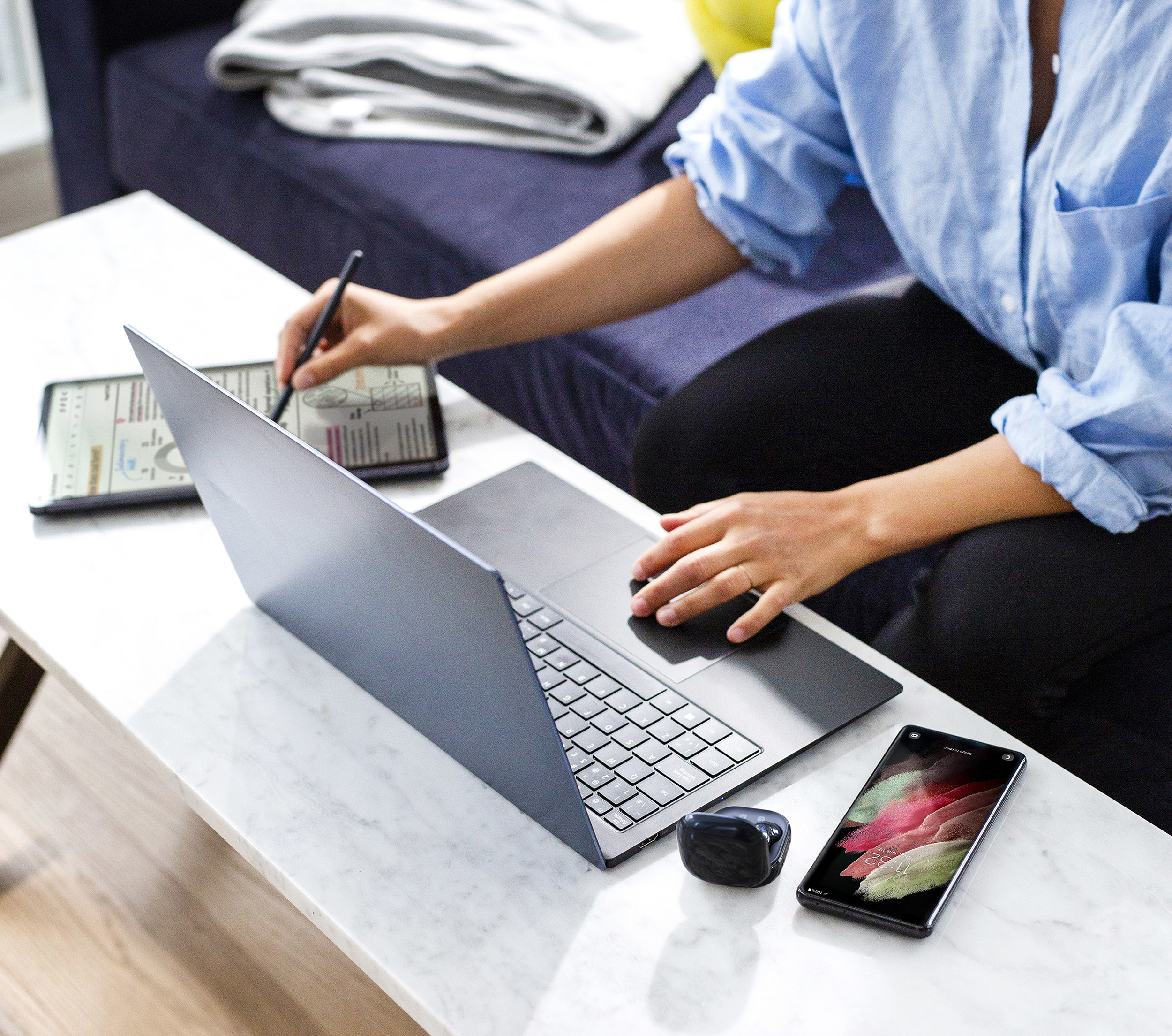 A person sitting on their couch working on a laptop and tablet