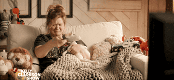 Kelly Clarkson sitting on a couch and crying then smiling while watching TV