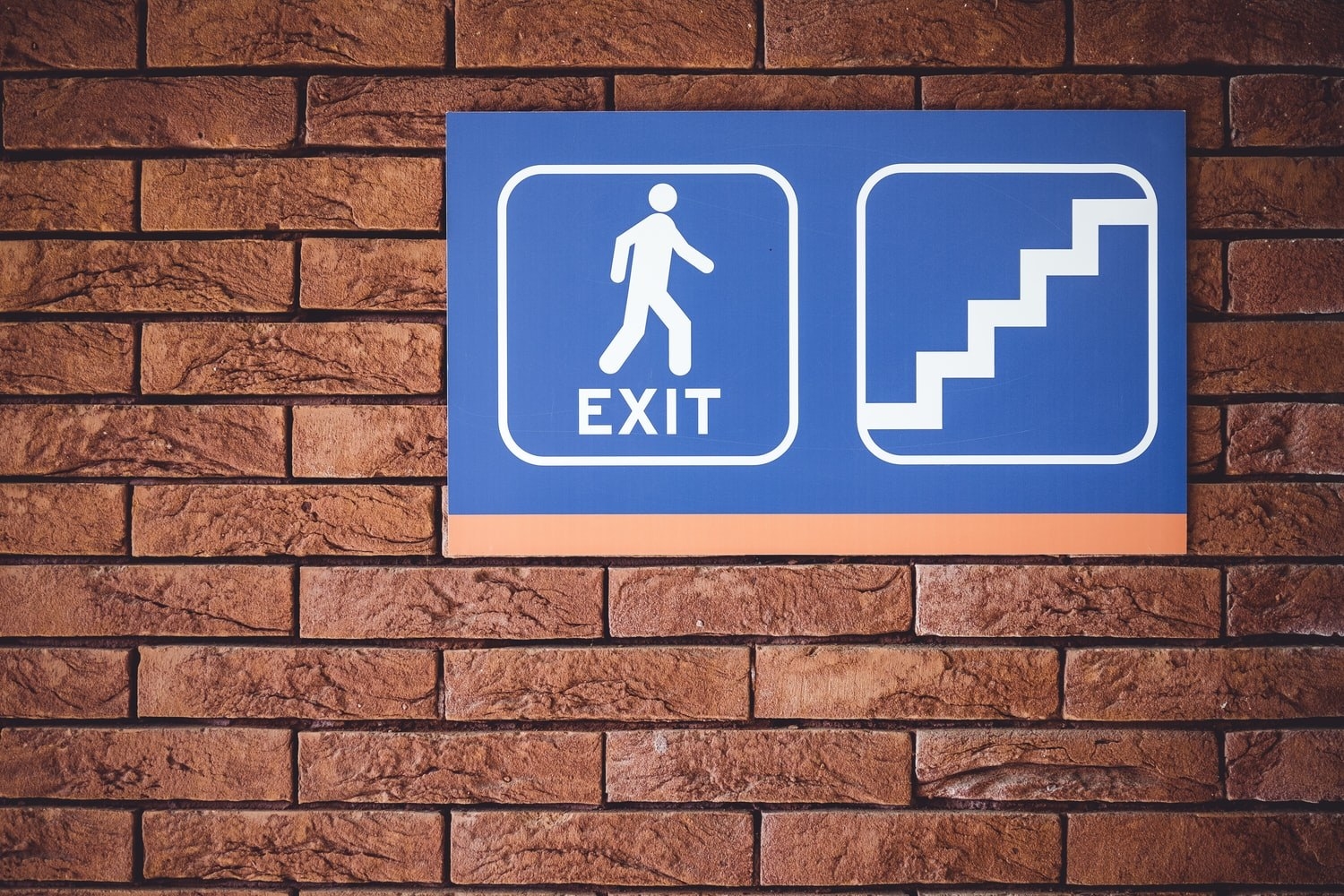 Brick wall with an &quot;Exit&quot; sign, a symbol of a personal exiting and a stairs symbol. 