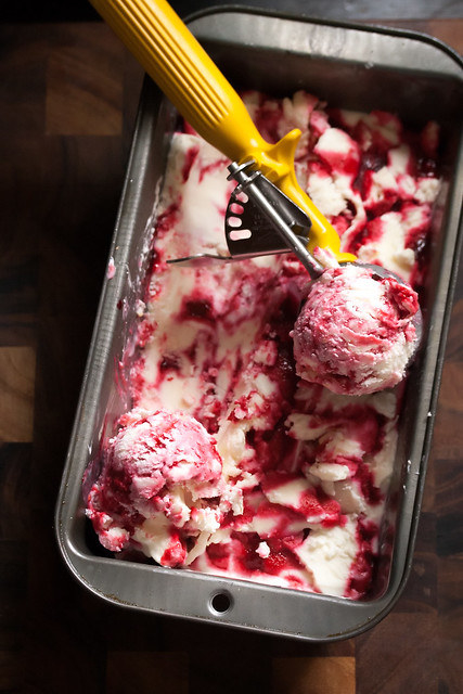 Raspberry ice cream being scooped from a metal pan.