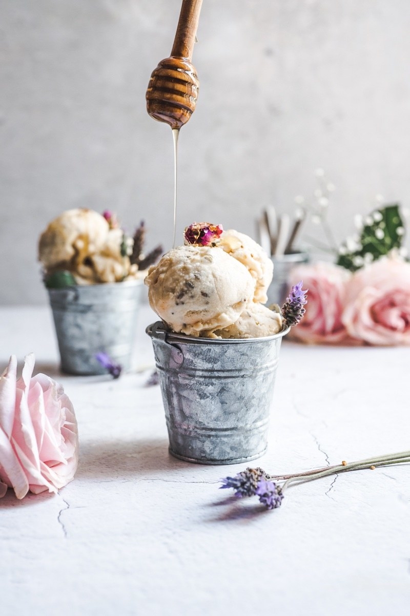 Scoops of ice cream in small metal pails next to roses and lavender.