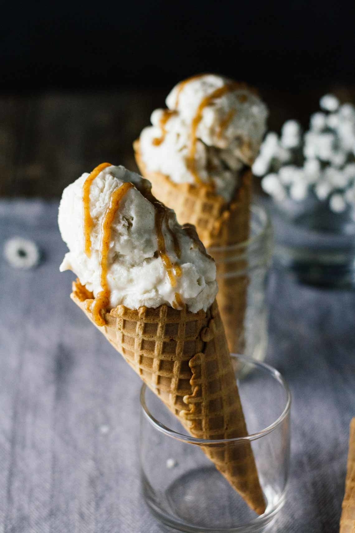 Scoop of ice cream drizzled with caramel on a cone in a glass cup.