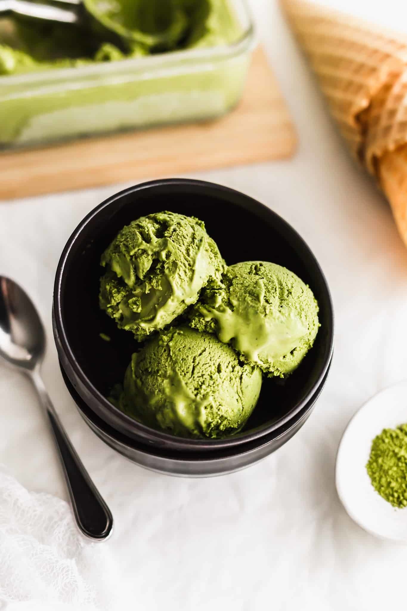 Three scoops of green ice cream in a black bowl next to a spoon.